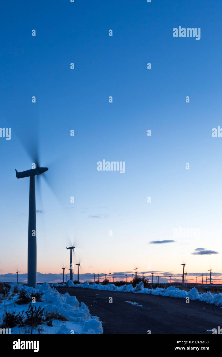 Wind Turbine movement on a cold winters day at sunset, with snow on the ground and an almost clear blue sky. Stock Photo