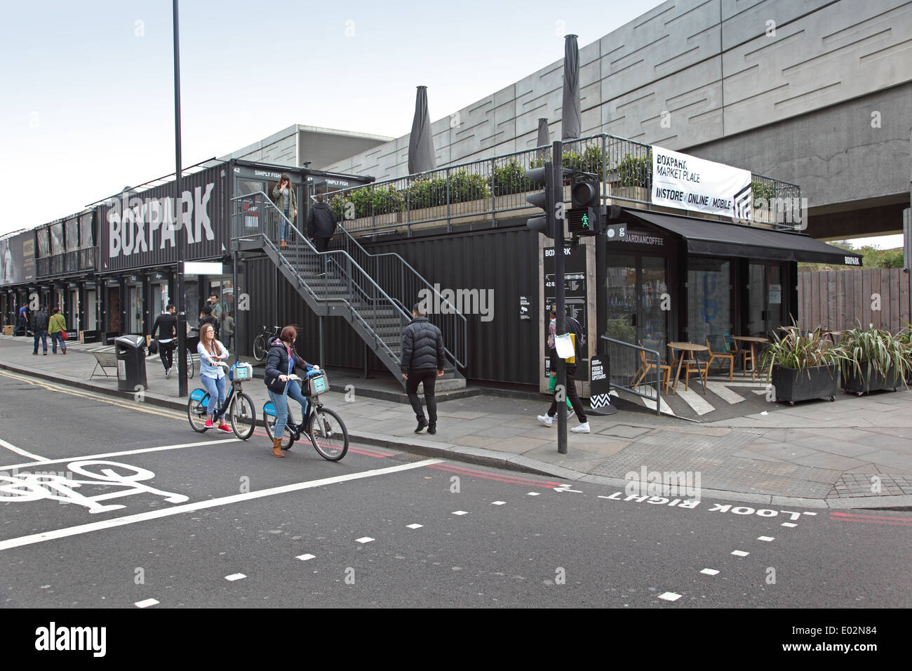 Boxpark. Pop-up shops and restaurants housed in shipping containers in Shoreditch, London. 2 girls on Boris-bikes in foreground Stock Photo