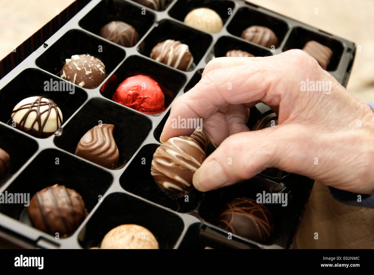Elderly woman helping herself to a chocolate from a box of chocolates Stock Photo