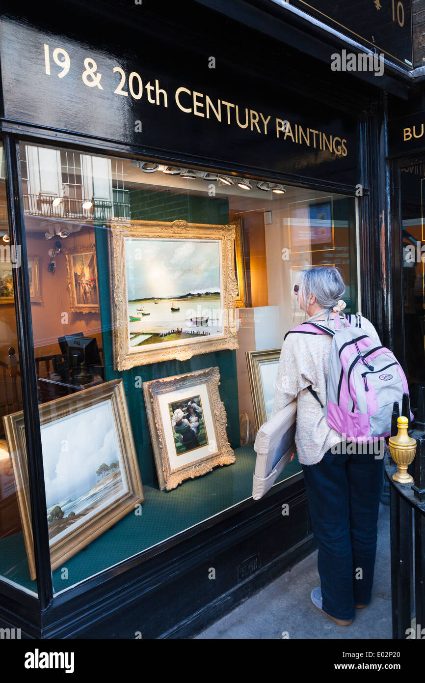 Woman carrying wrapped painting looking in gallery window. Stock Photo