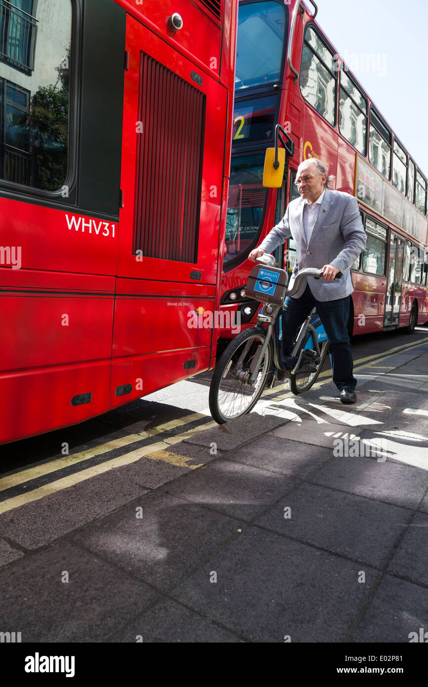 Man on bicycle squeezing between London Bus and curb. Stock Photo