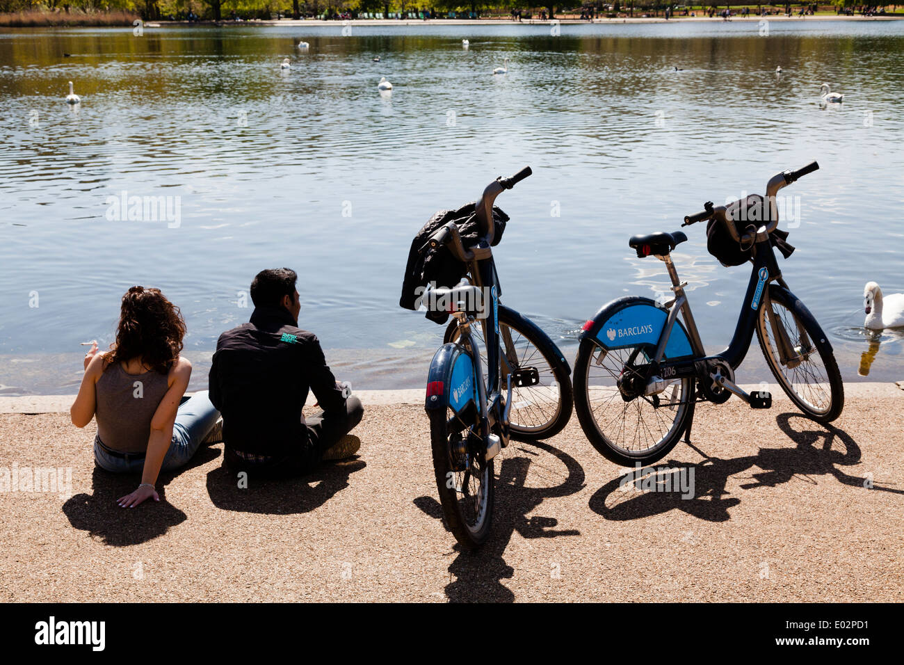 Couple with Barclays London Cycle Hire bicycles resting by the Serpentine in Hyde Park. Stock Photo
