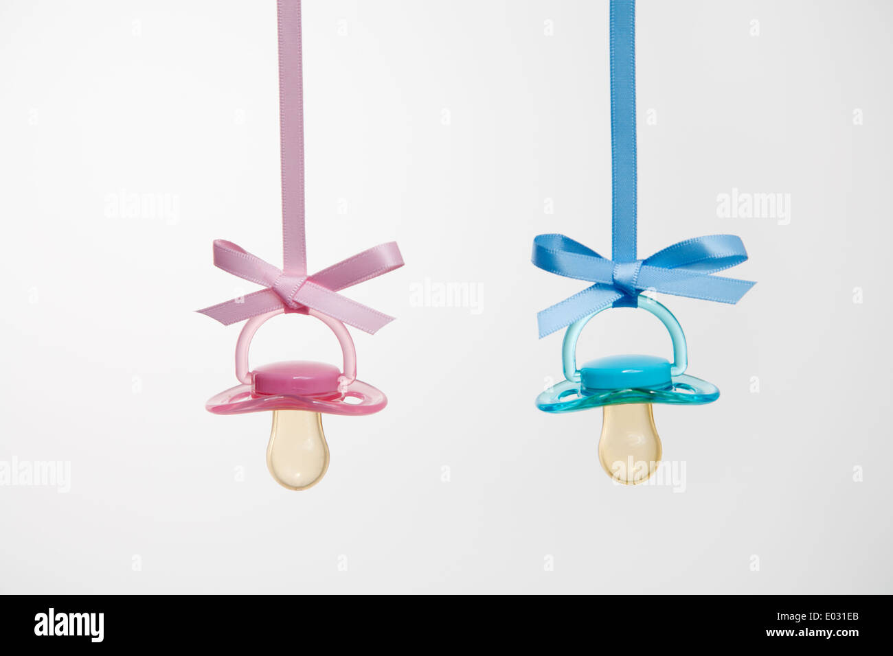 Baby pacifiers hanging from ribbons against a plain background. Stock Photo