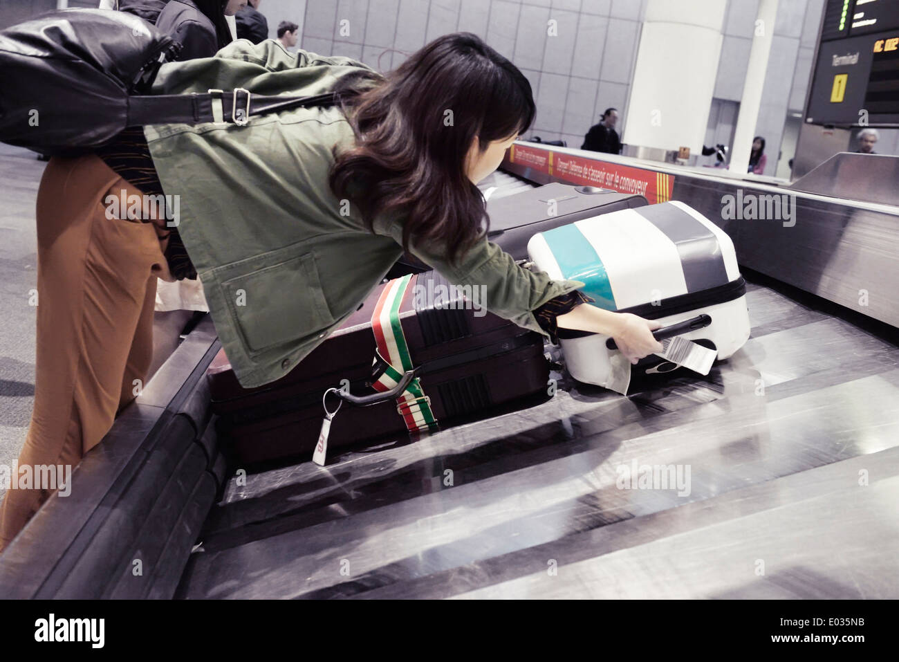 Woman picking up suitcase from airport baggage conveyor at Toronto Pearson International airport luggage claim, Canada Stock Photo