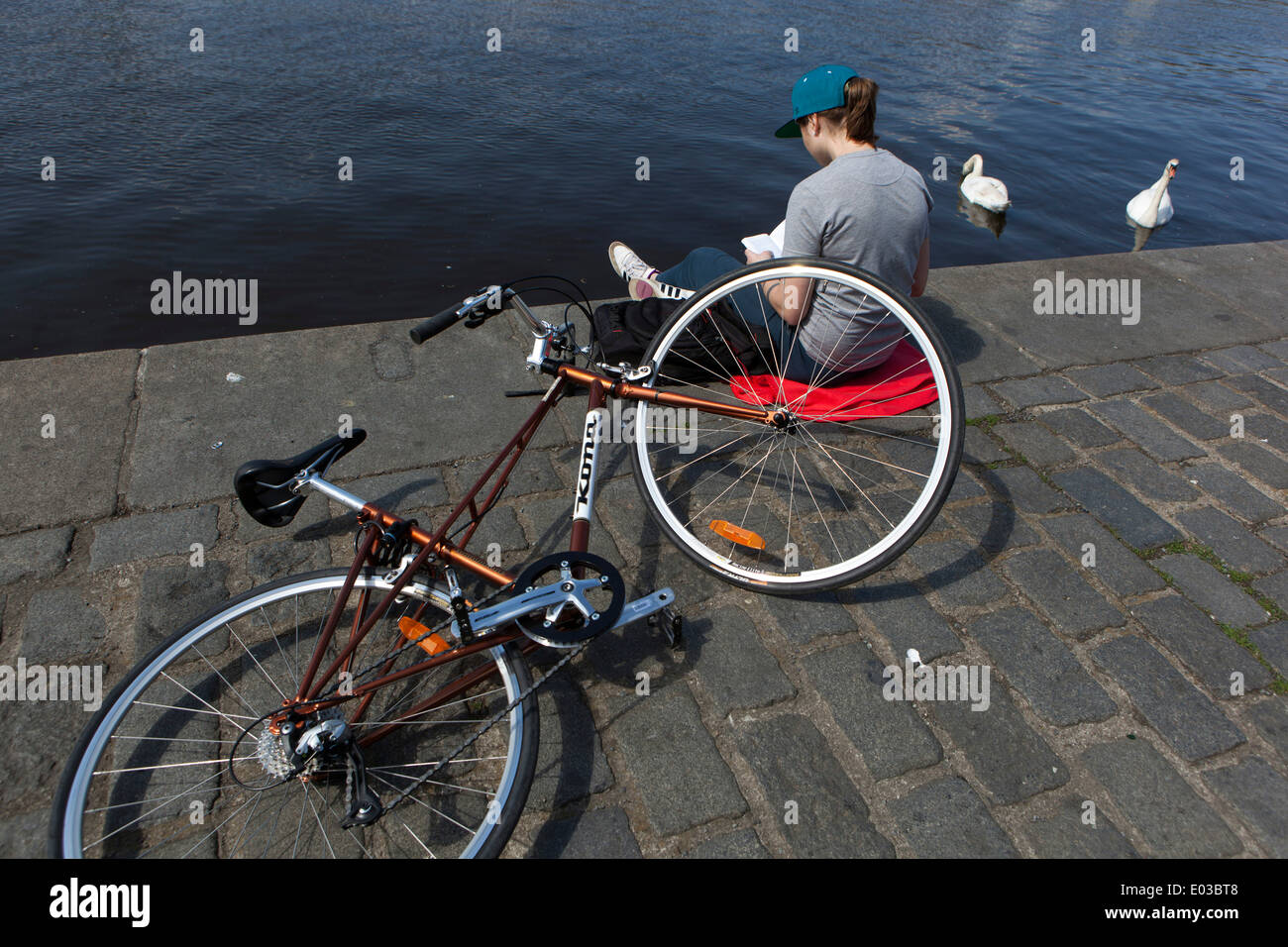 A young teenager reading a book, bike river swan Prague riverside outside Stock Photo