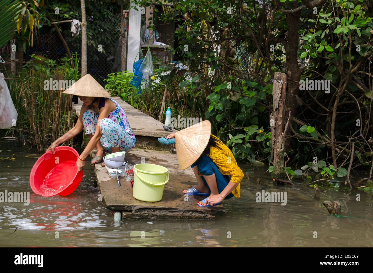 Two women washing bowls on banks of a river in the Mekong Delta, Vietnam Stock Photo