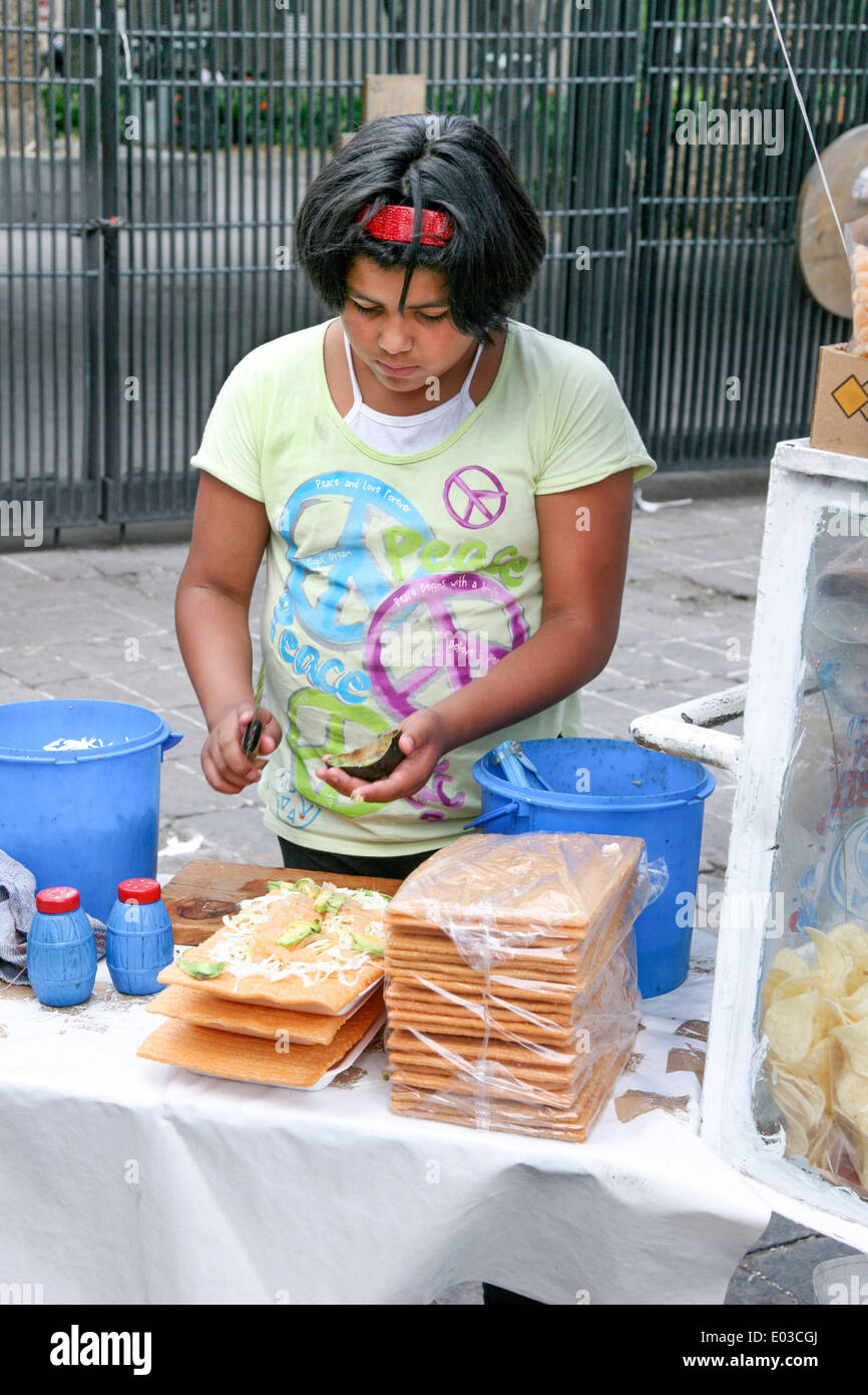 pretty Mexican pre teen slicing fresh avocado onto deep fried Chicharron shell at food stall outside Chapultepec park entrance Stock Photo