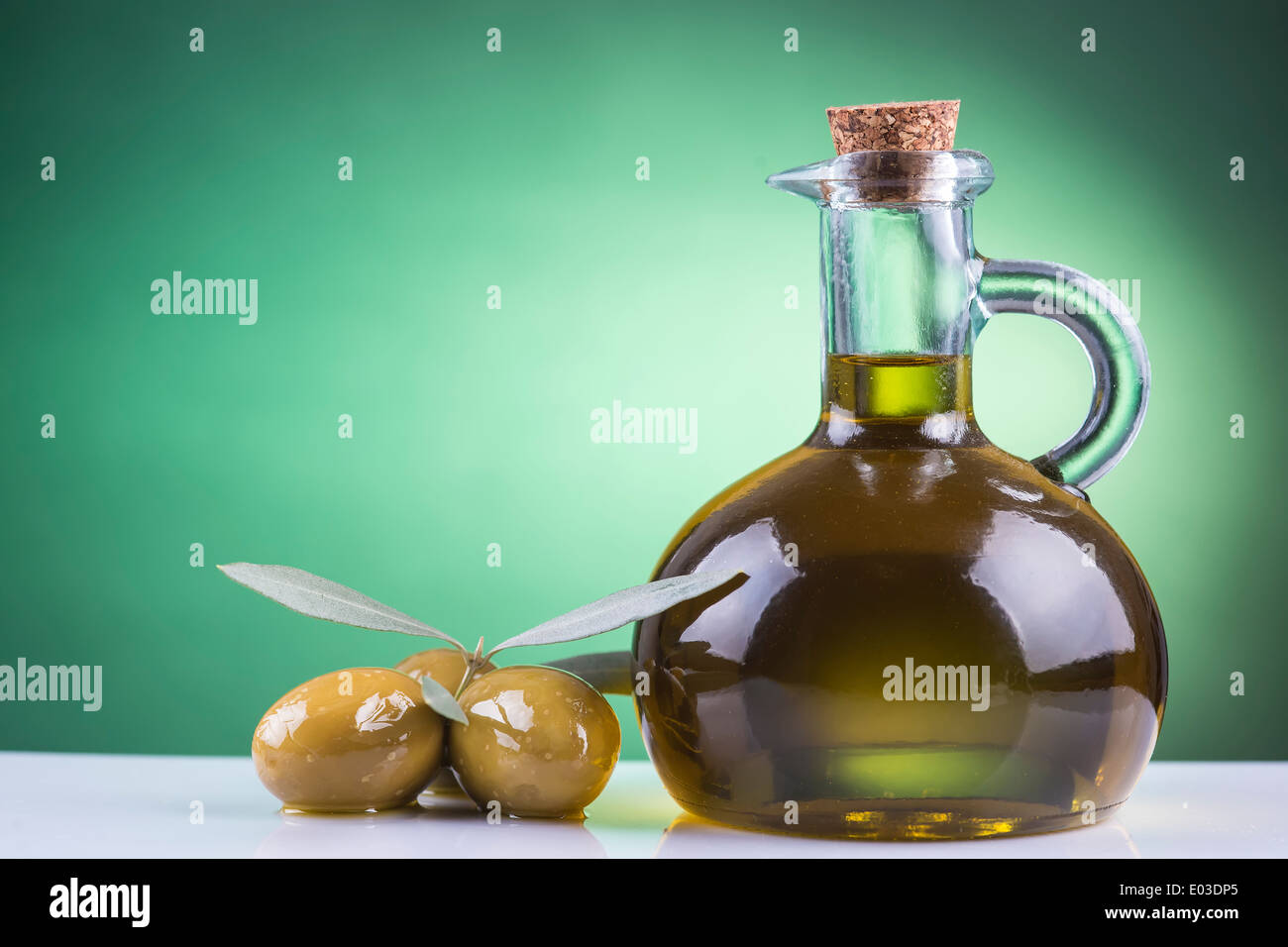 Olive oil bottle and olives on a green spotlight background Stock Photo