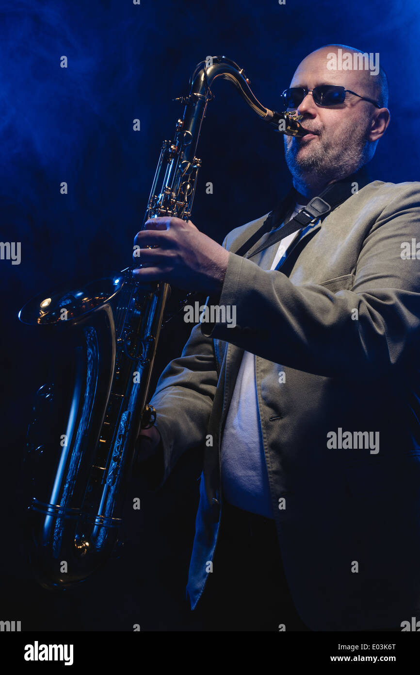 Adult musician playing tenor saxophone, blue smoky background Stock