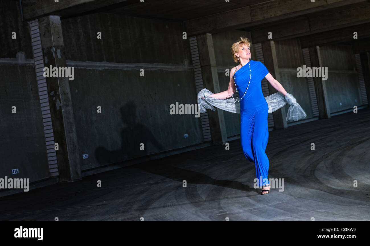 Frightened woman wearing blue dress and running in the public parking house Stock Photo
