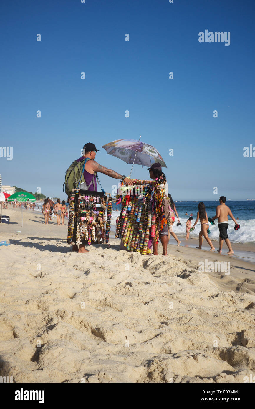 RIO DE JANEIRO, BRAZIL - JANUARY 22, 2014: Two beach vendors stand with their wares talking on Ipanema Beach. Stock Photo