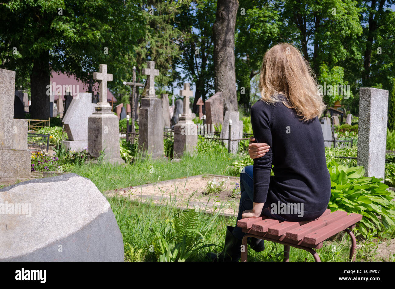 Sorrow woman shrinked near father husband tomb in cemetery. Stock Photo
