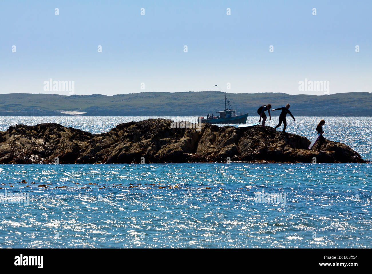 Children playing on rocks on a beach on Isle of Coll Inner Hebrides Argyll and Bute Scotland UK with fishing boat in background Stock Photo