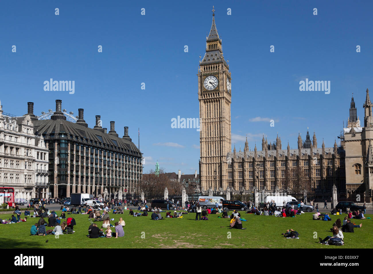 Tourists sitting on the grass of Parliament Square with Big Ben and the Houses of Parliament London. Stock Photo