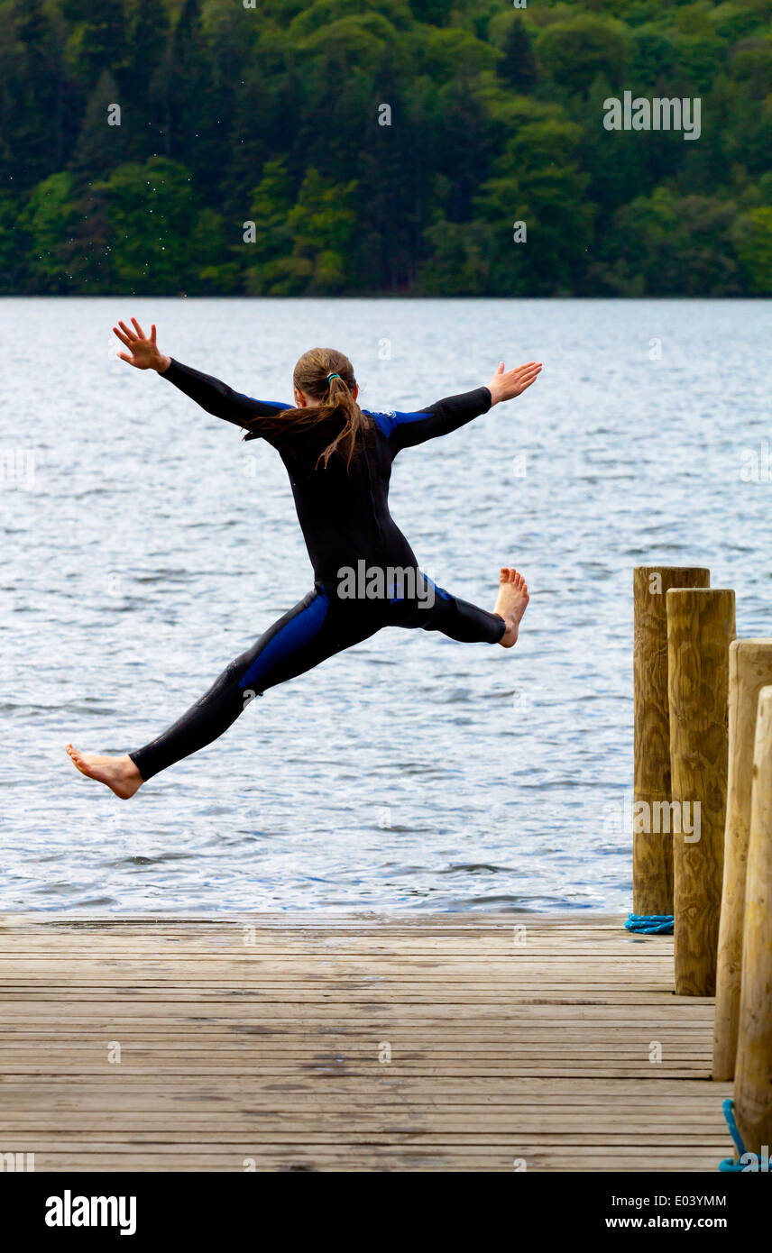 Twelve year old girl in wetsuit jumping off wooden jetty into Lake