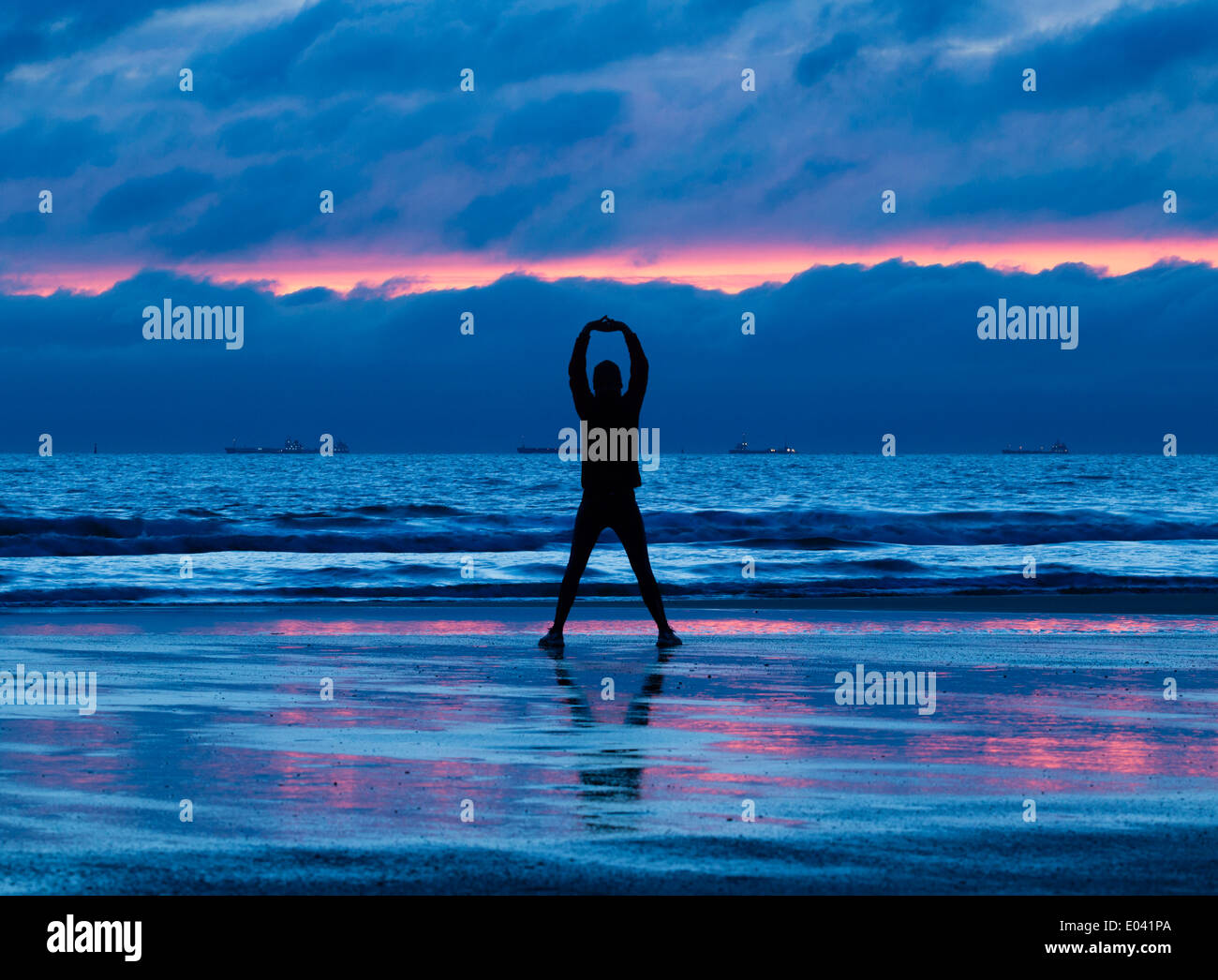 Jogger stretching on beach at sunrise Stock Photo