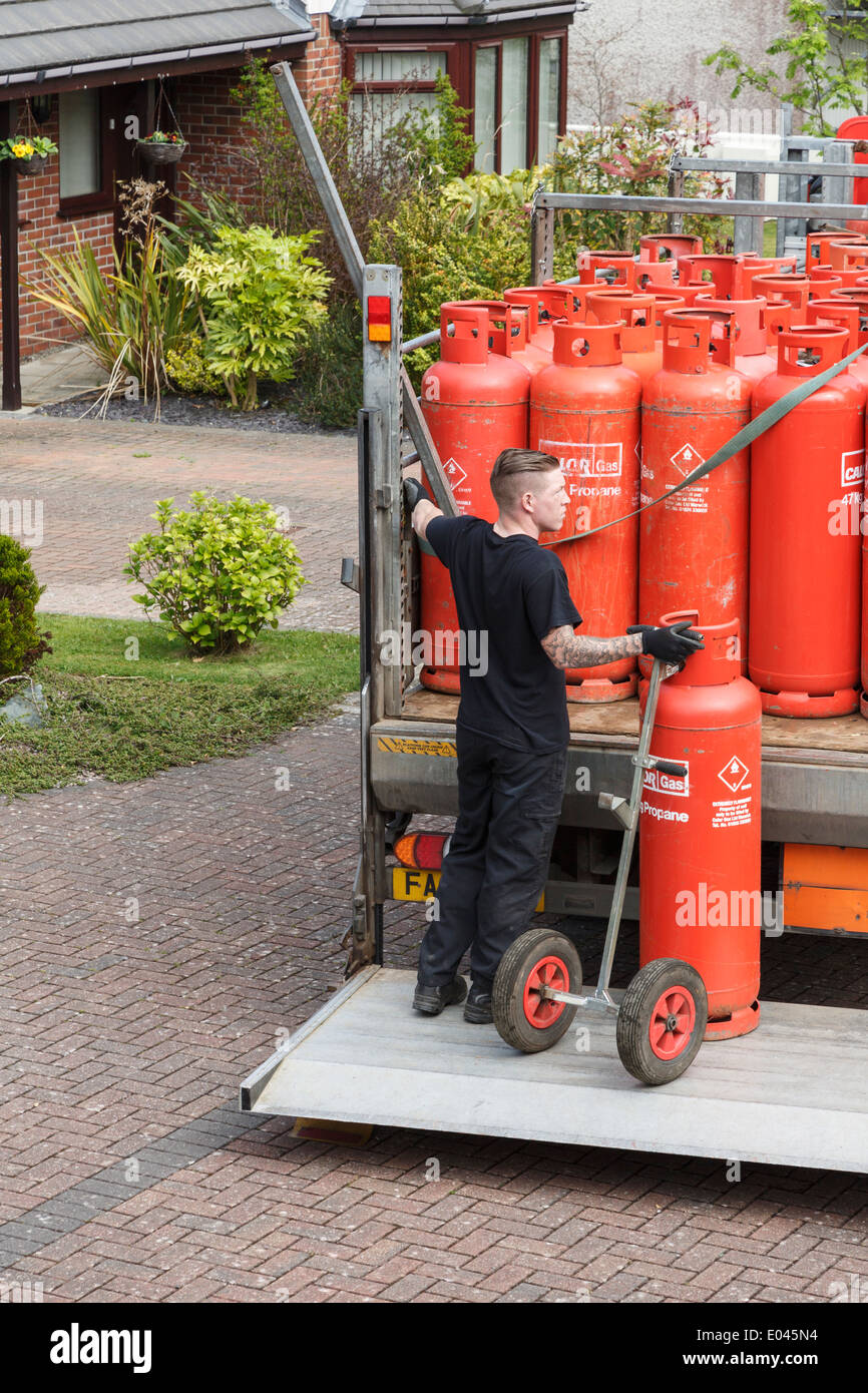 A delivery man delivering household red Calor Gas bottles on a pickup truck tail lift outside a house. North Wales, UK, Britain Stock Photo