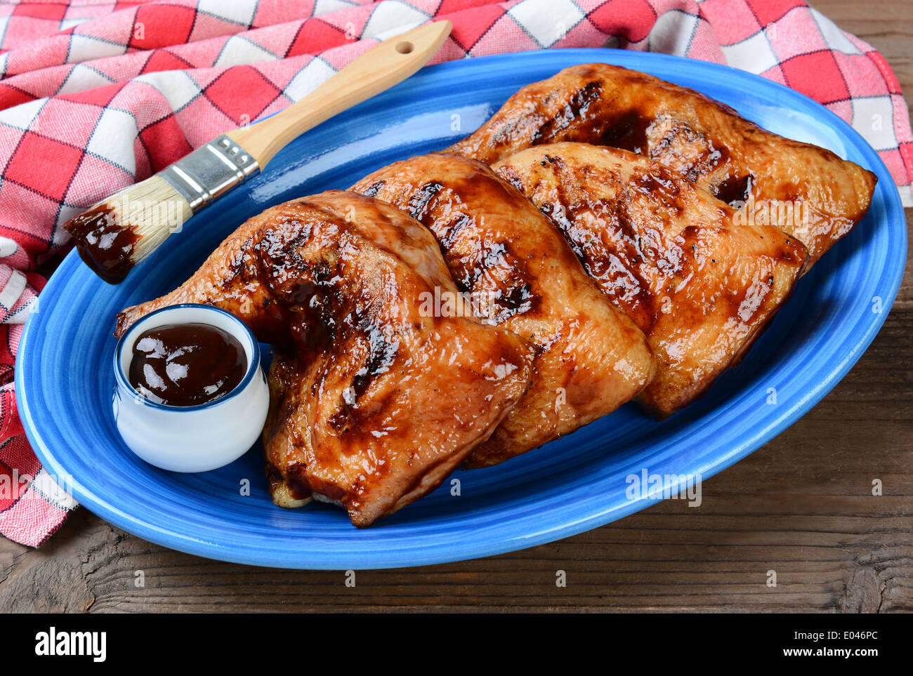 High angle shot of chicken leg quarters on a blue oval platter. The legs have been barbecued and are coated in sauce Stock Photo