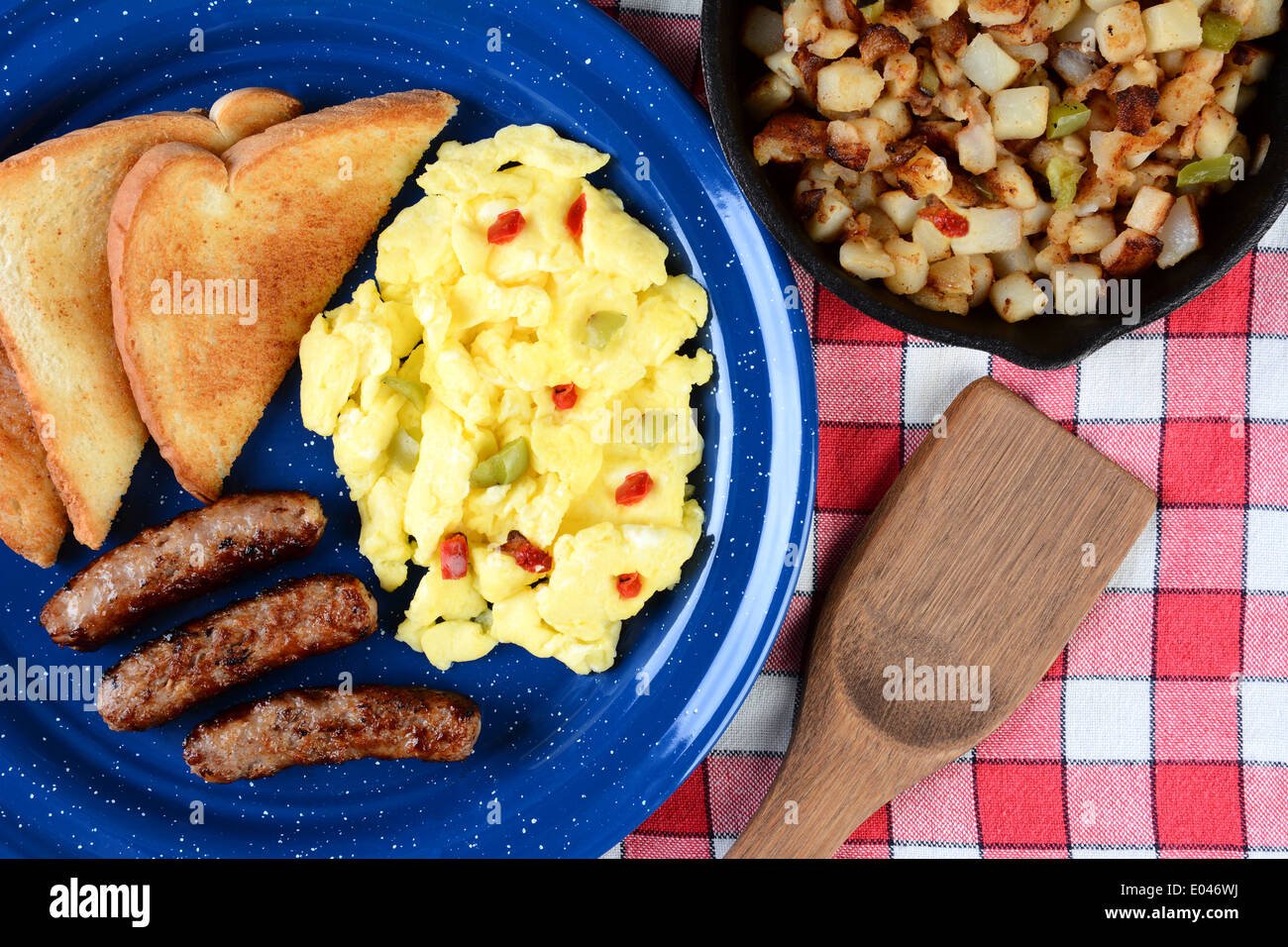 High angle shot of country style scrambled eggs with peppers, sausage and toast. The breakfast is on a rustic wooden table Stock Photo