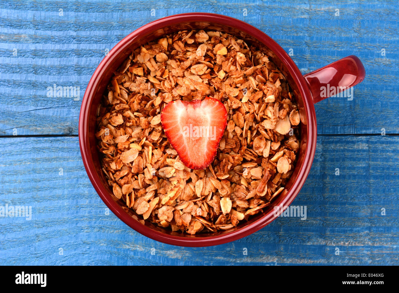 High angle shot of a large mug filled with healthy whole grain cereal with a single sliced strawberry in the middle. Stock Photo