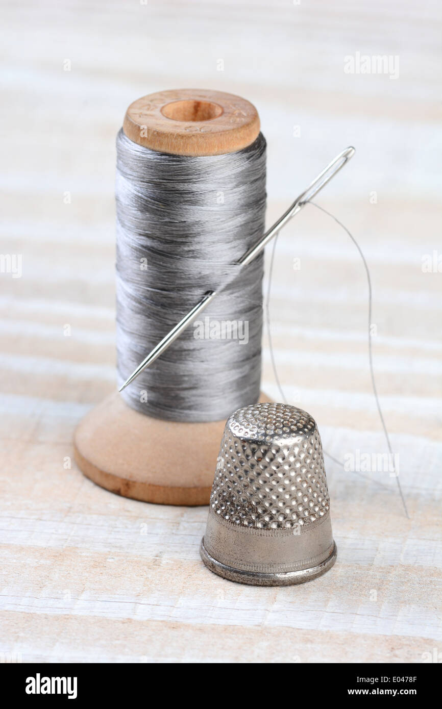 Closeup of an antique thimble and thread spool. A needle sticks through the thread on an old fashioned wooden spool. Stock Photo