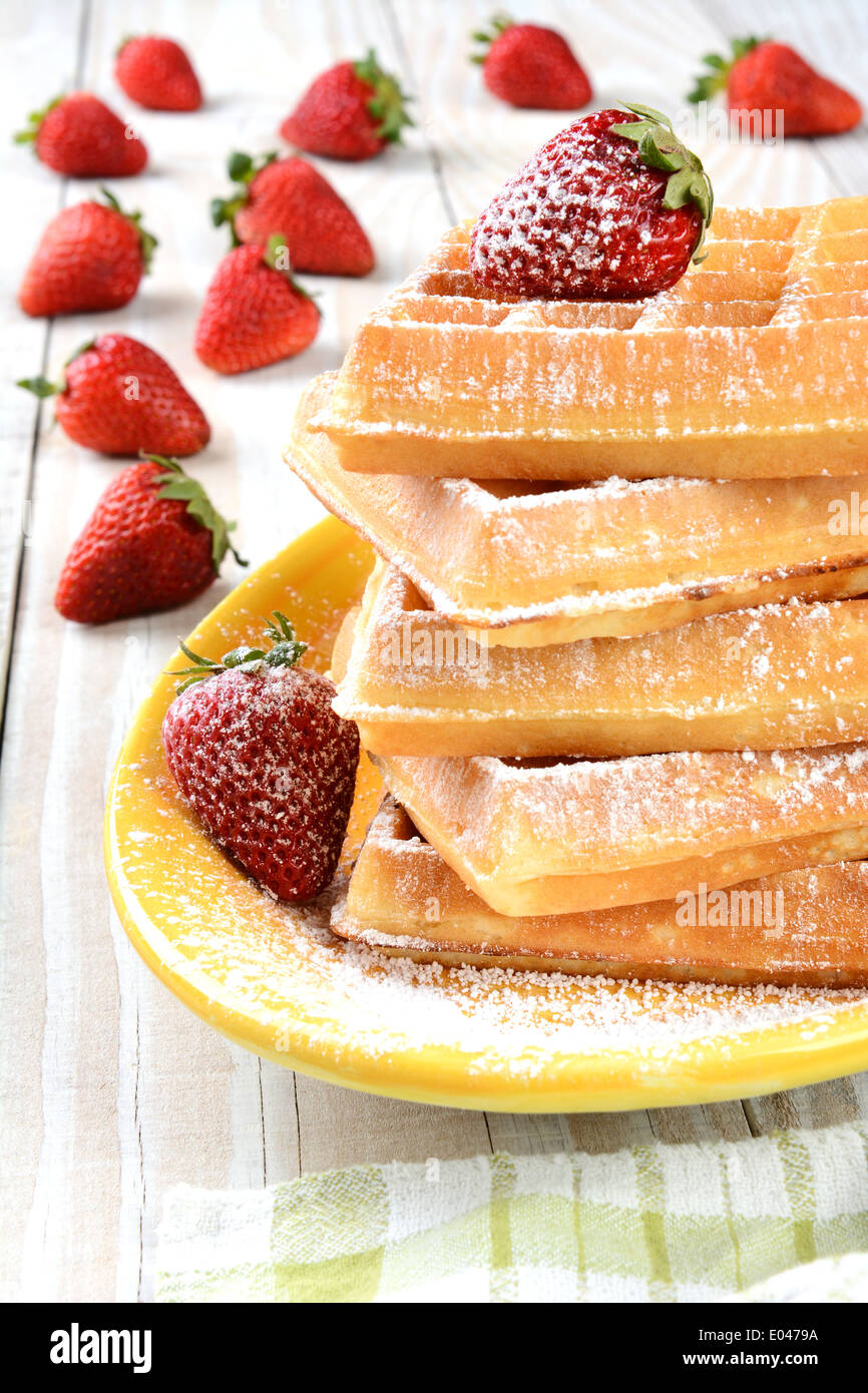Waffles and strawberries covered with powdered sugar. The stack of waffles is on a yellow platter Stock Photo
