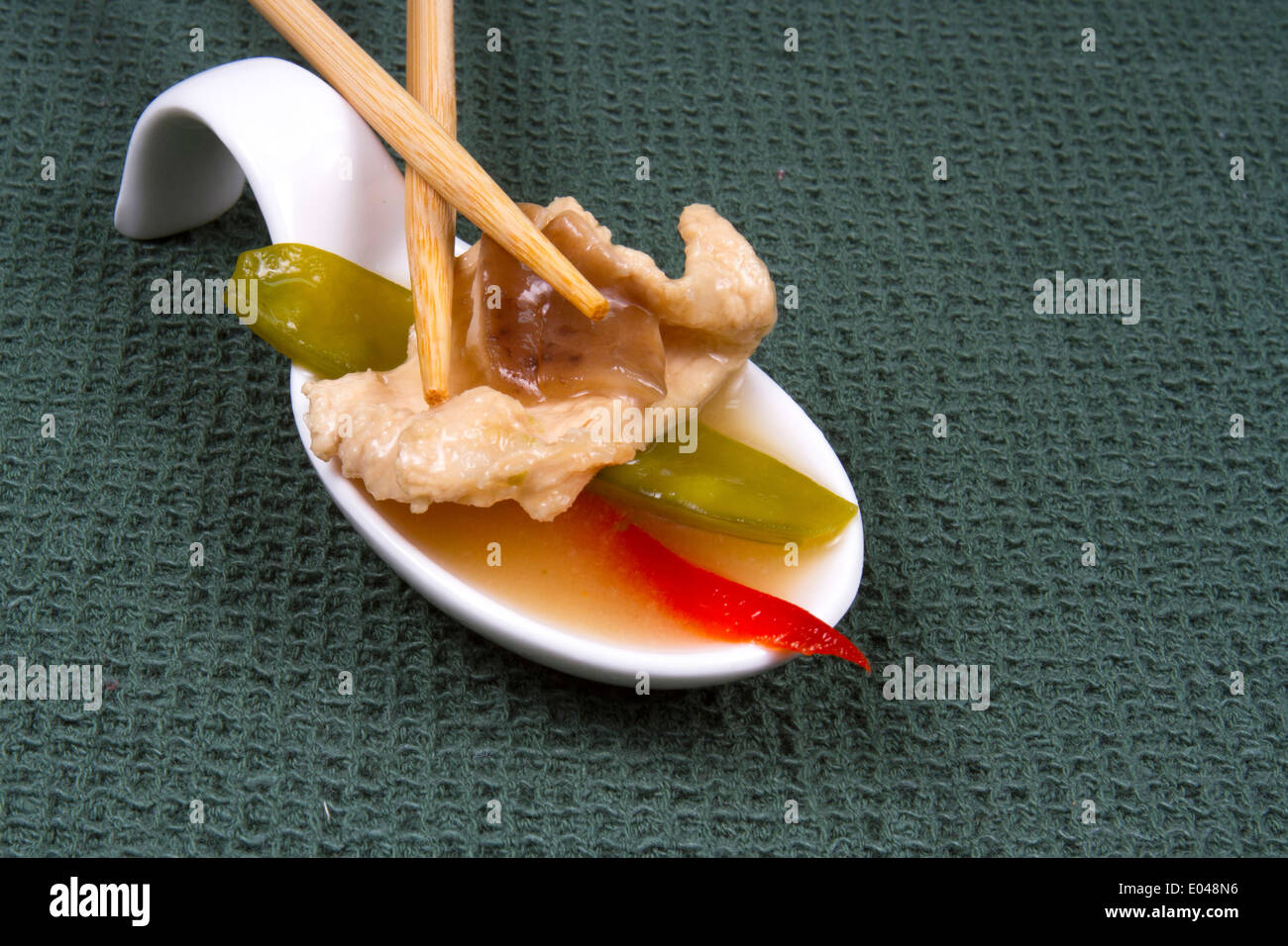 Single bite of Asian Chicken Soup with red pepper and snow peas with chopsticks on green linen Stock Photo