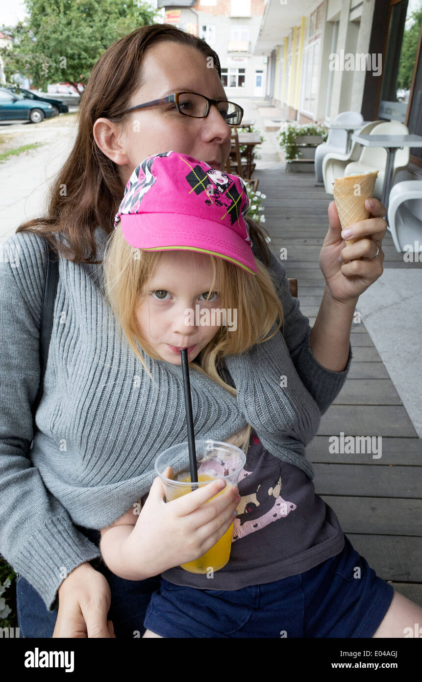 Chilly daughter wrapped inside mom's sweater sipping her orange juice thru a straw age 6 and 34. Rawa Mazowiecka Central Poland Stock Photo