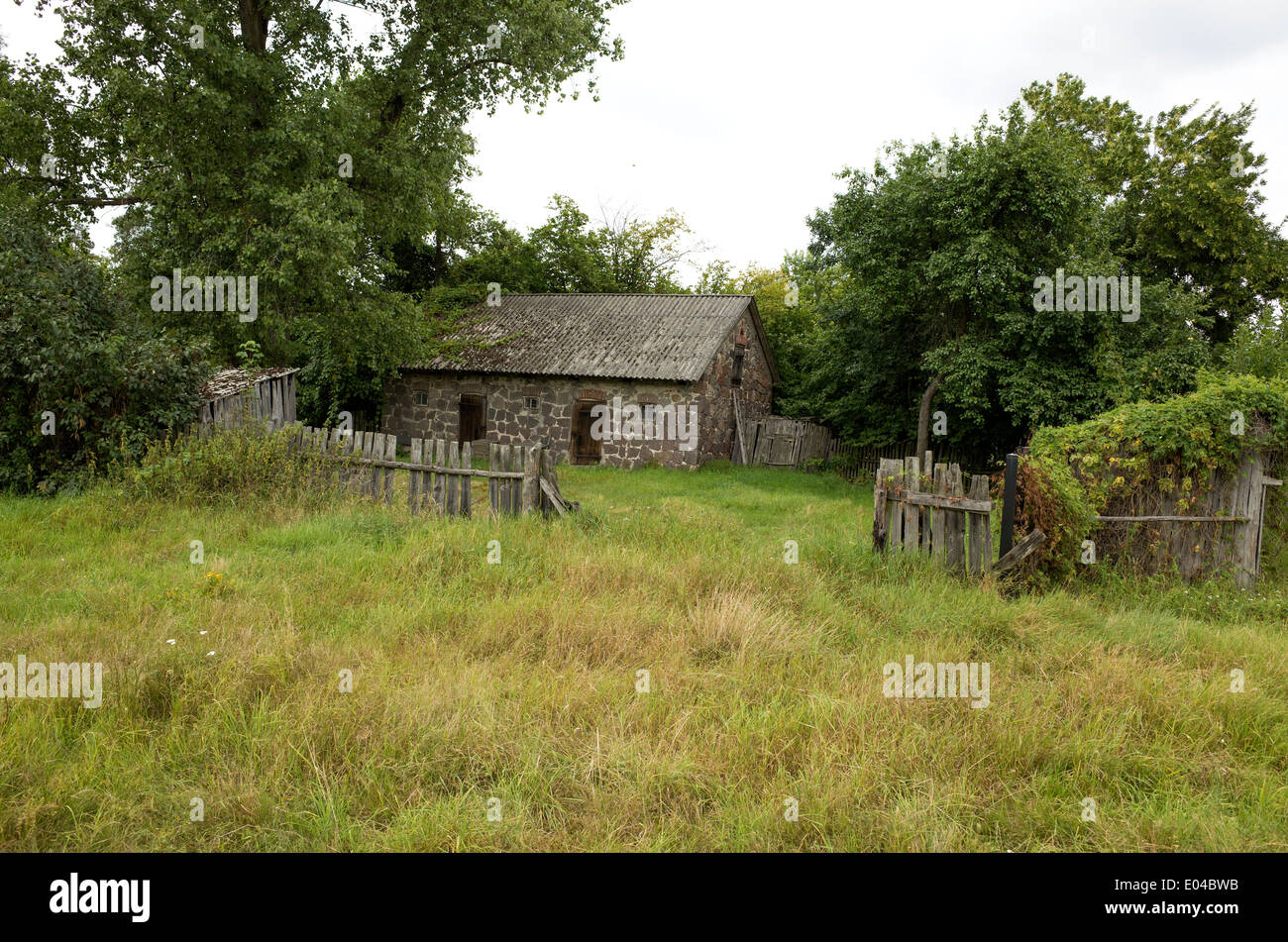 Vintage Polish farm building made of cut stone with rustic wood fence. Zawady Central Poland Stock Photo