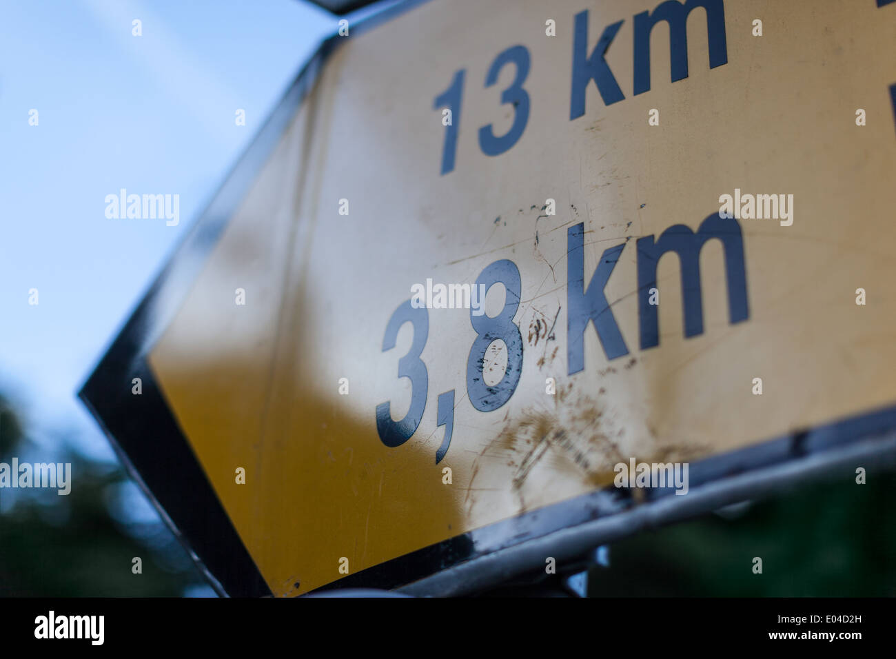 a worn and scratched road sign indicating the distance of 13 and 3,8 km Stock Photo