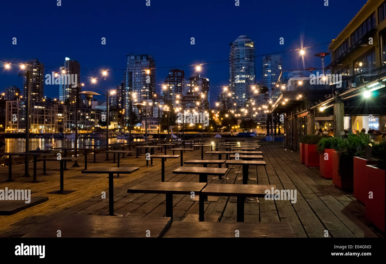 Empty tables on an outdoor patio of a restaurant on Granville Island in Vancouver, at night.  City lights buildings and marina. Stock Photo