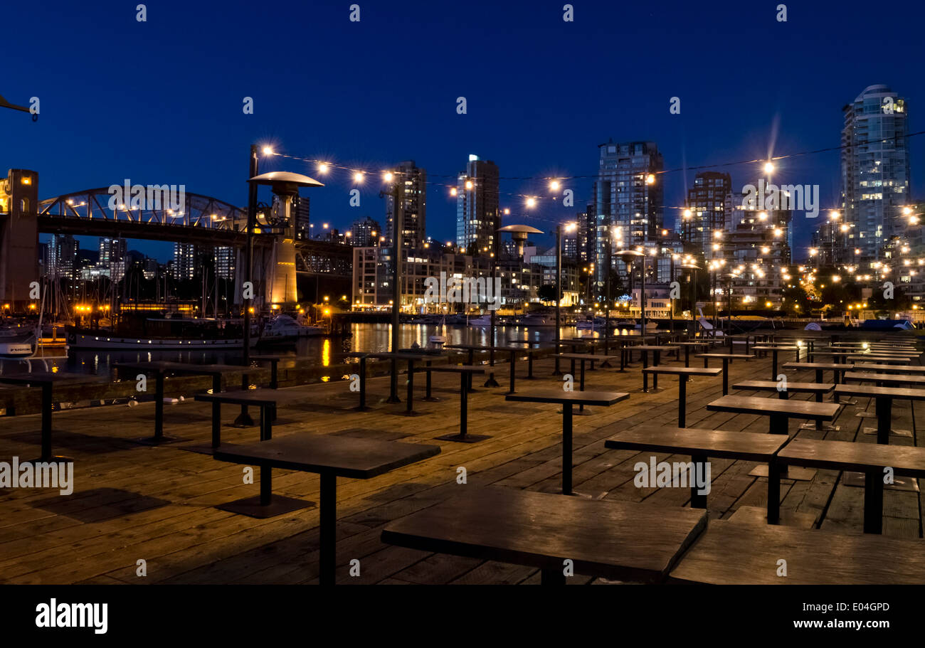 Empty patio tables outside a restaurant on Granville Island, Vancouver at night.  Lights of the city and Burrard Street Bridge. Stock Photo