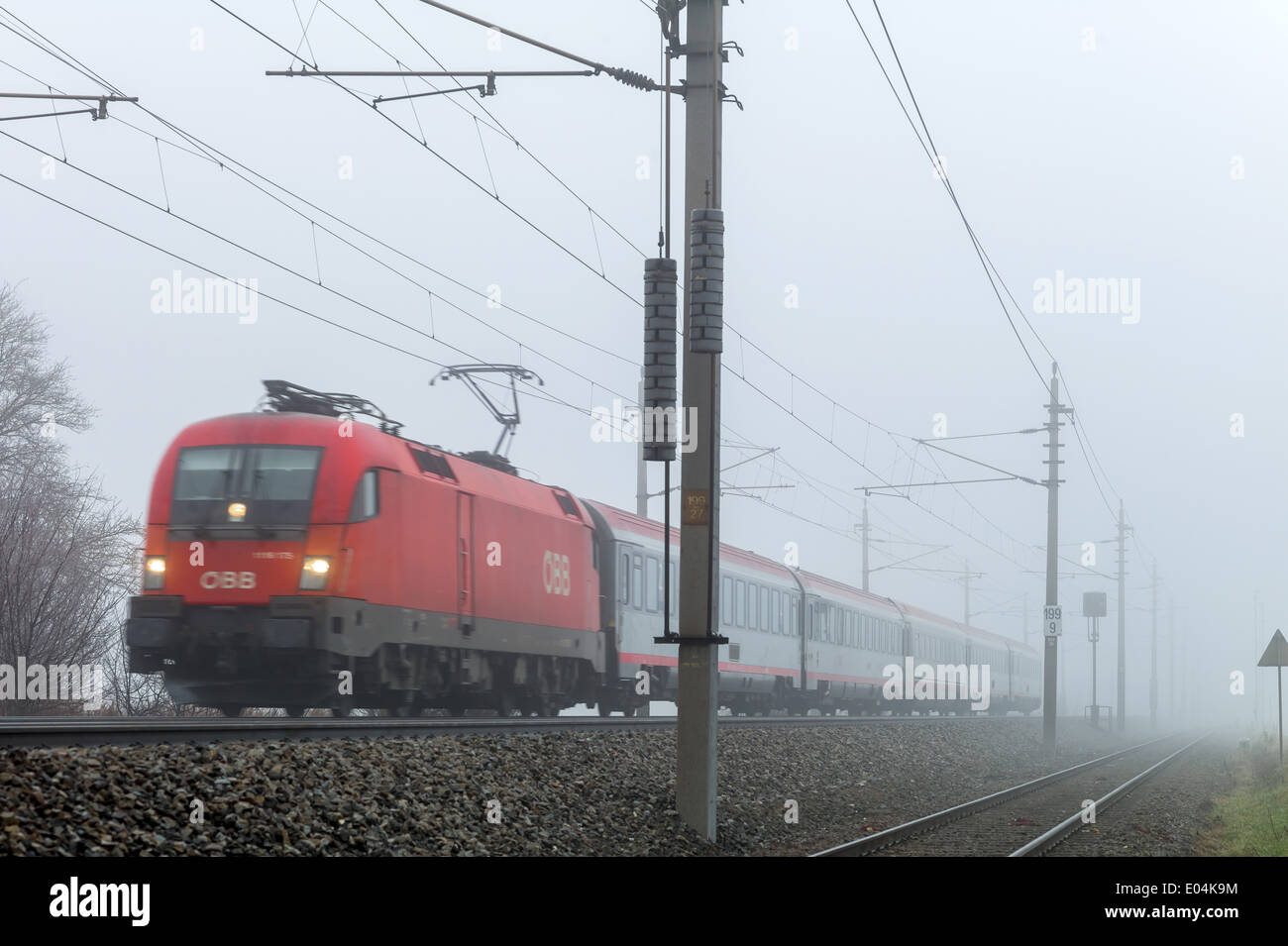 A railroad engine by a stopping train of the ?BB in the fog., Eine Lokomotive mit einem Personenzug der OeBB im Nebel. Stock Photo