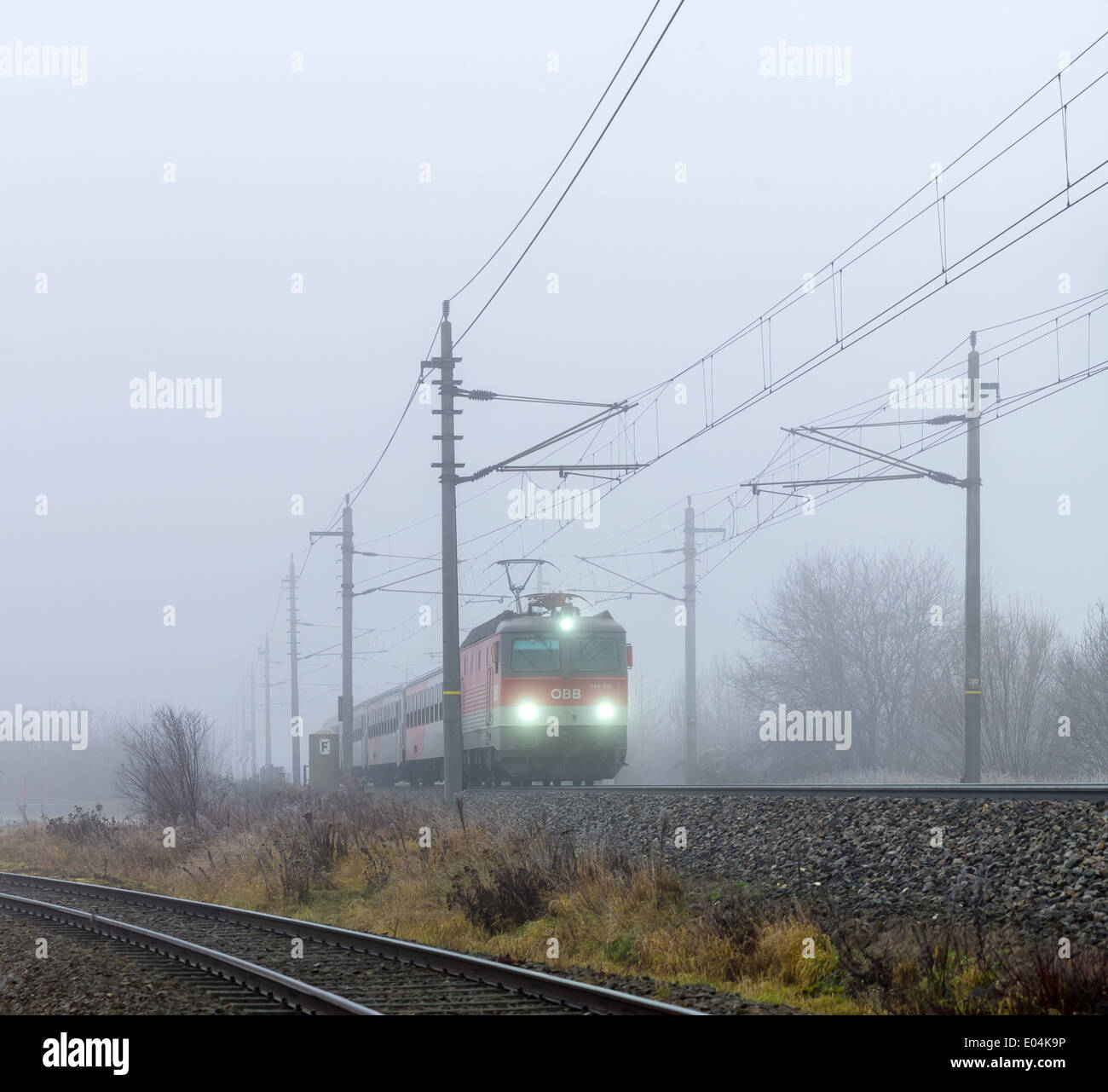 A railroad engine by a stopping train of the ?BB in the fog., Eine Lokomotive mit einem Personenzug der OeBB im Nebel. Stock Photo