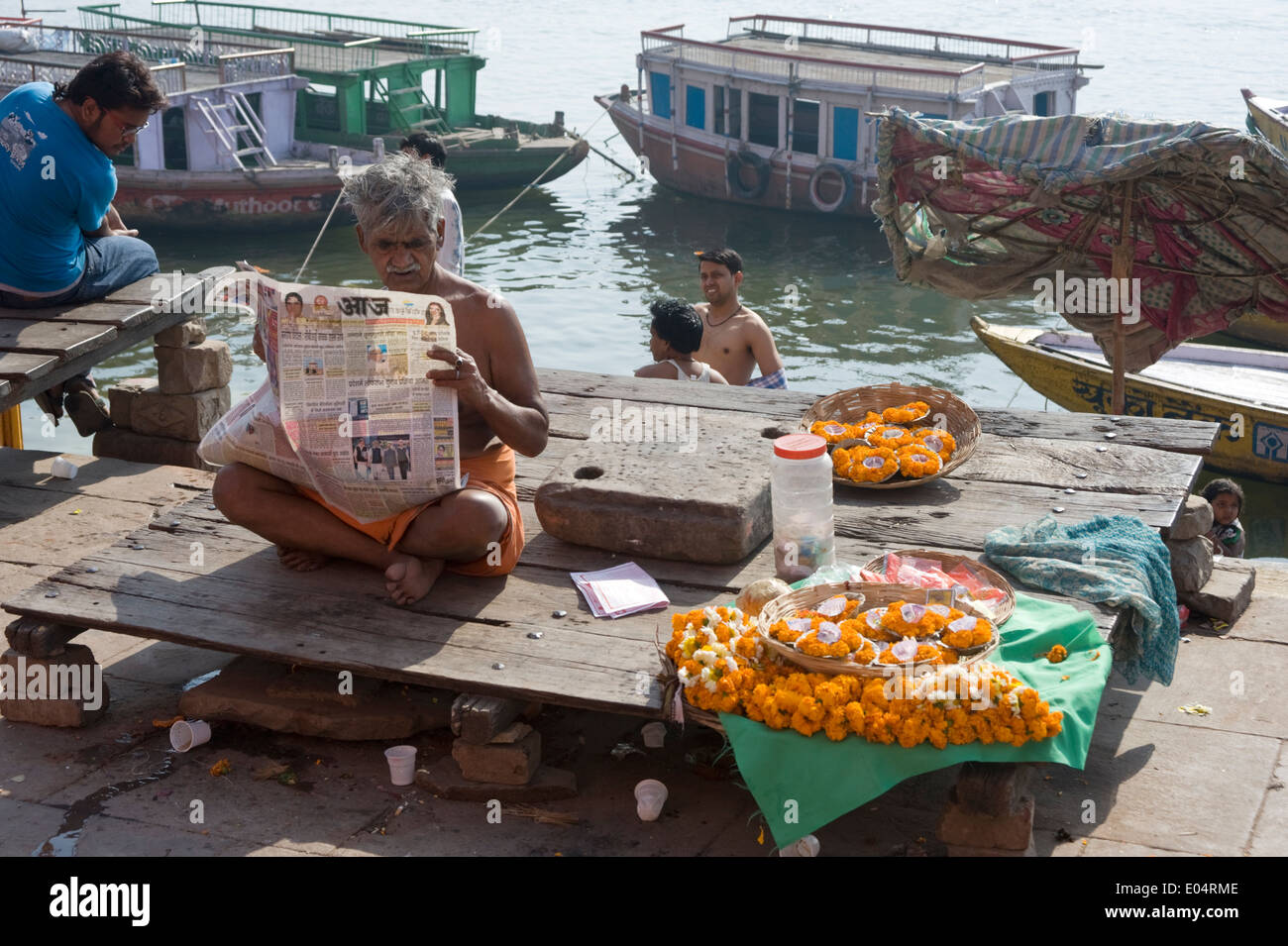 Brahmin priest reading newspaper by the Ganges, Varanasi, India Stock Photo