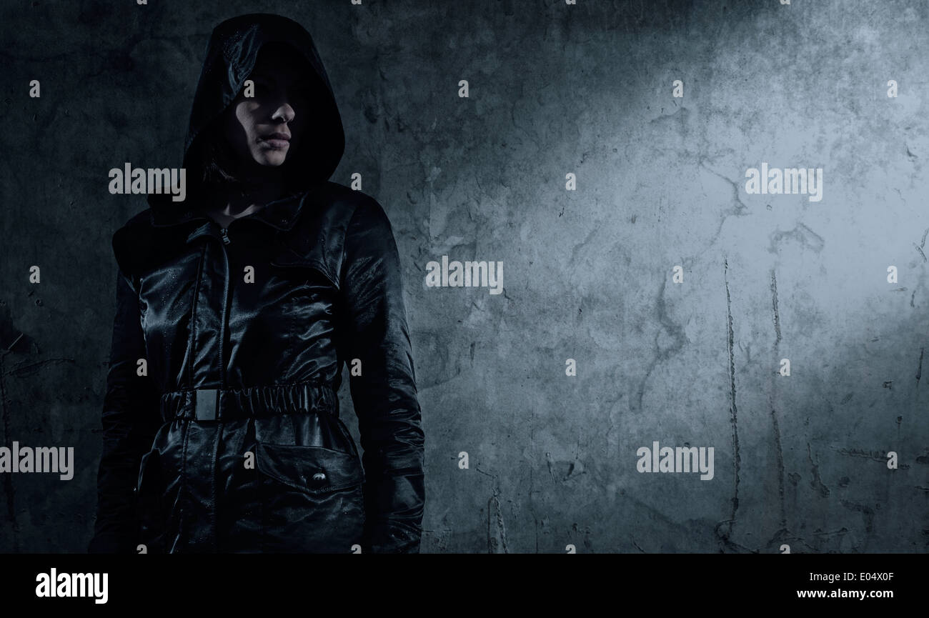 Woman in dark hooded jacket next to wall Stock Photo