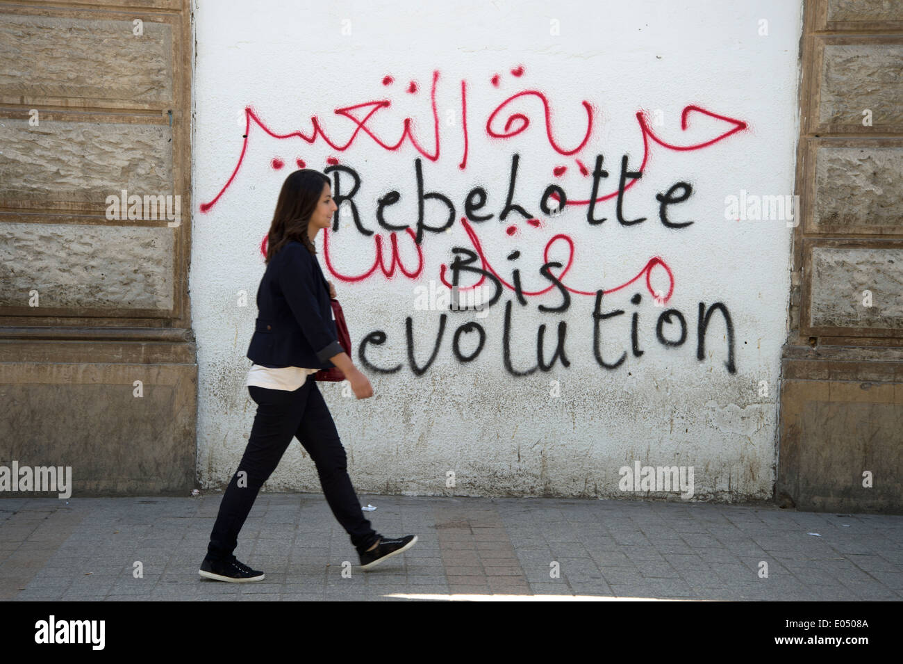 Tunisia 2014. A woman wearing jeans walks past  slogans saying revolution written on a wall Stock Photo