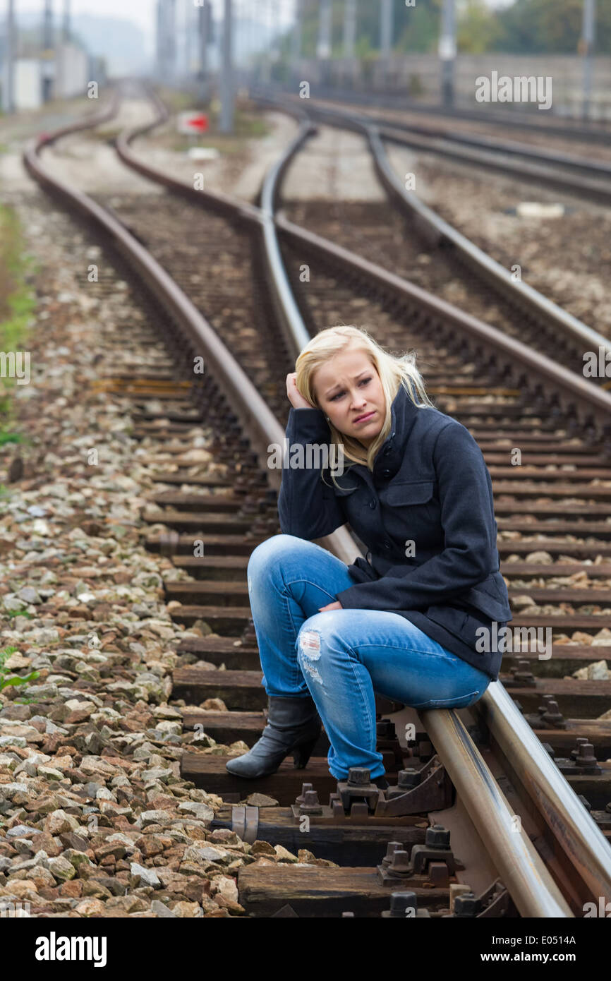 A young woman is sad, afraid and depressed. Sits on a rail and is lonesome, Eine junge Frau ist traurig, aengstlich und deprimie Stock Photo
