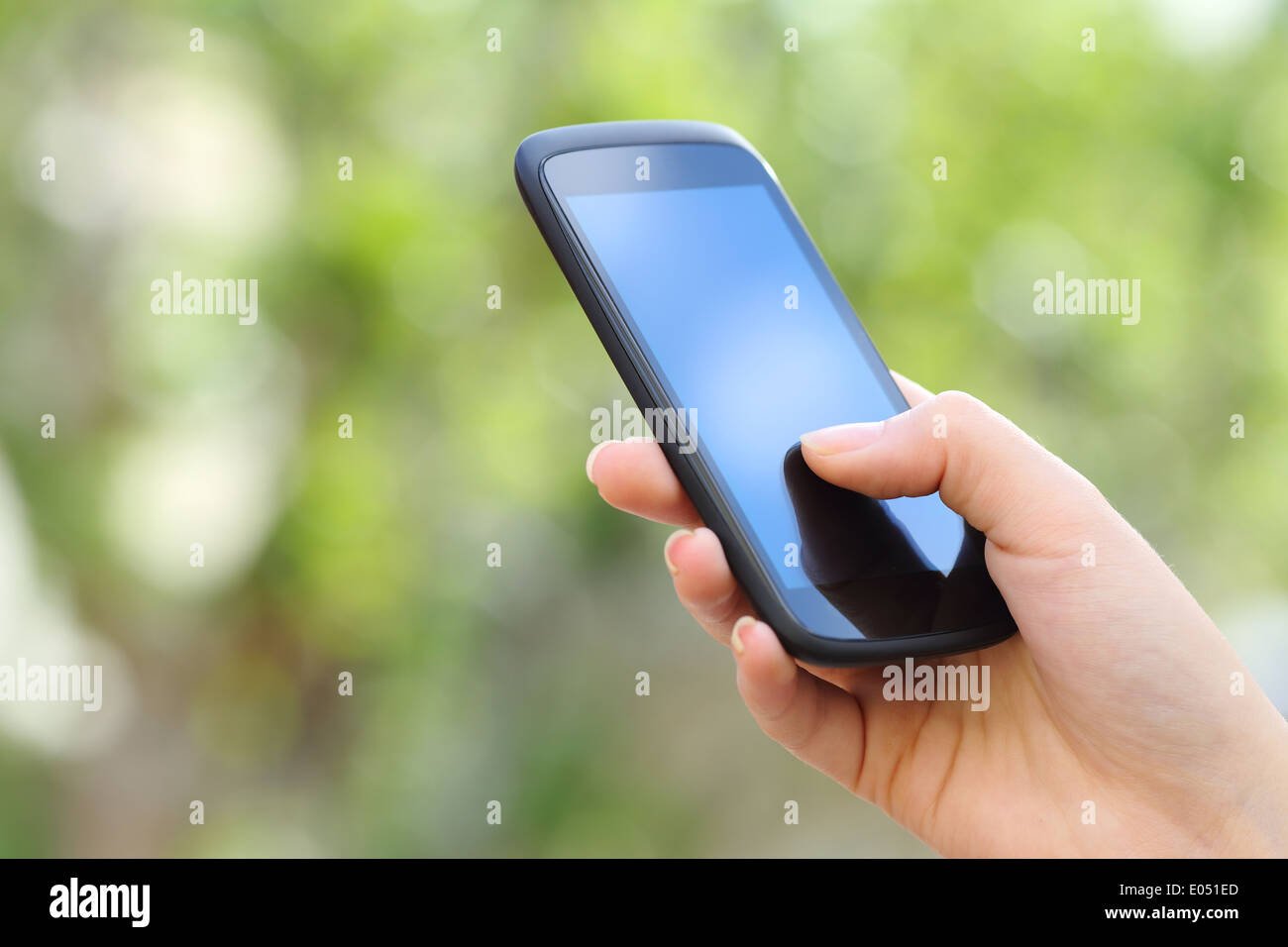 Woman hand holding a smart phone outdoor with a green background Stock Photo