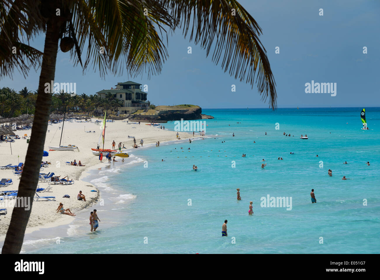 Coconut palm tree and Xanadu mansion at white sand beach of Varadero resort Cuba with tourists in turquoise water of the Atlantic Ocean Stock Photo