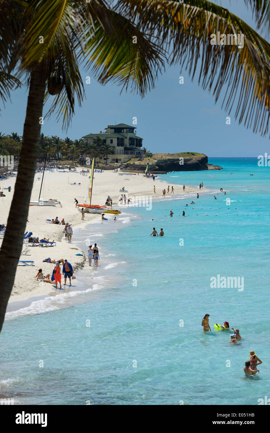 Swimmers on beach with coconut palm tree over turquoise ocean and Xanadu mansion at Varadero resort Cuba Stock Photo