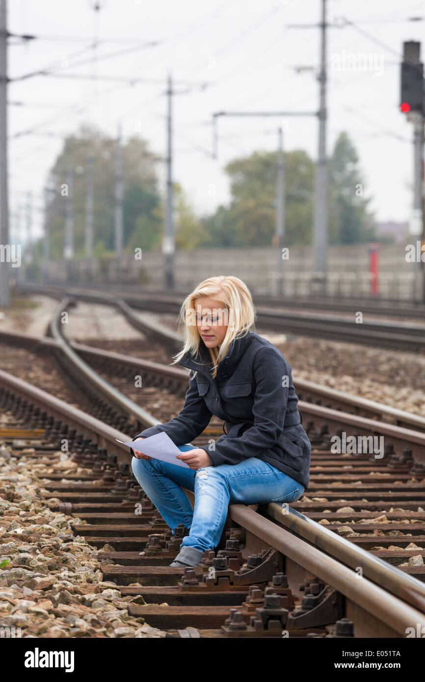 A young woman with suicide thoughts sits on a rail. If farewell letter holds in the hand and thinks about her suicide., Eine jun Stock Photo