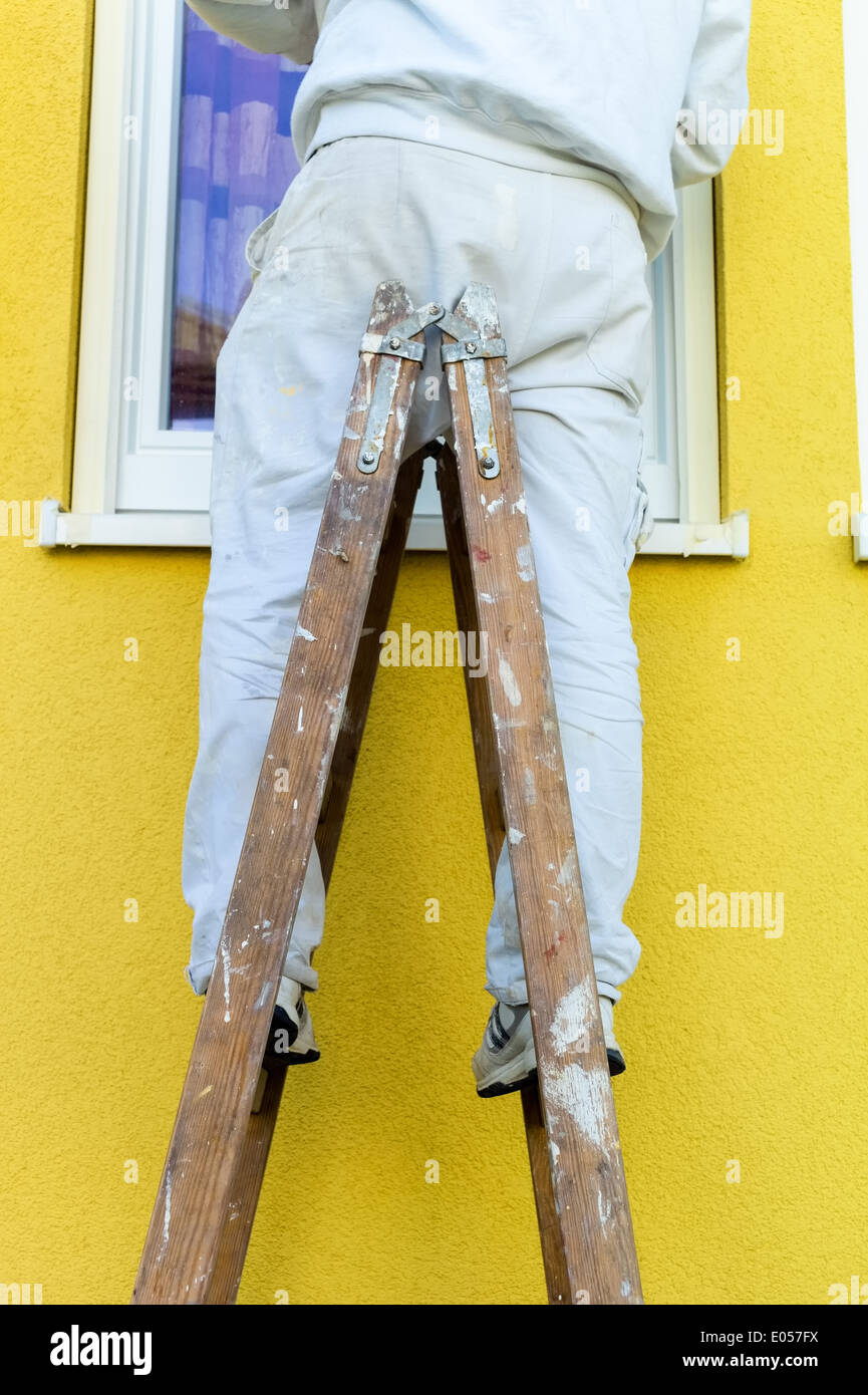 A painter on a step ladder. House facade is stroked. Renovate and redevelop, Ein Maler auf einer Stehleiter. Hausfassade wird ge Stock Photo