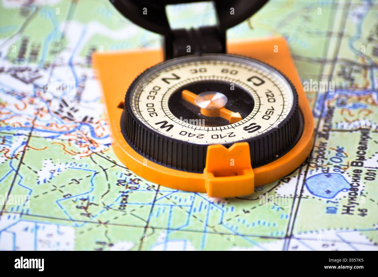 Topographic map lies on a white background, and there is a magnetic compass in a black case on an orange ground. Stock Photo