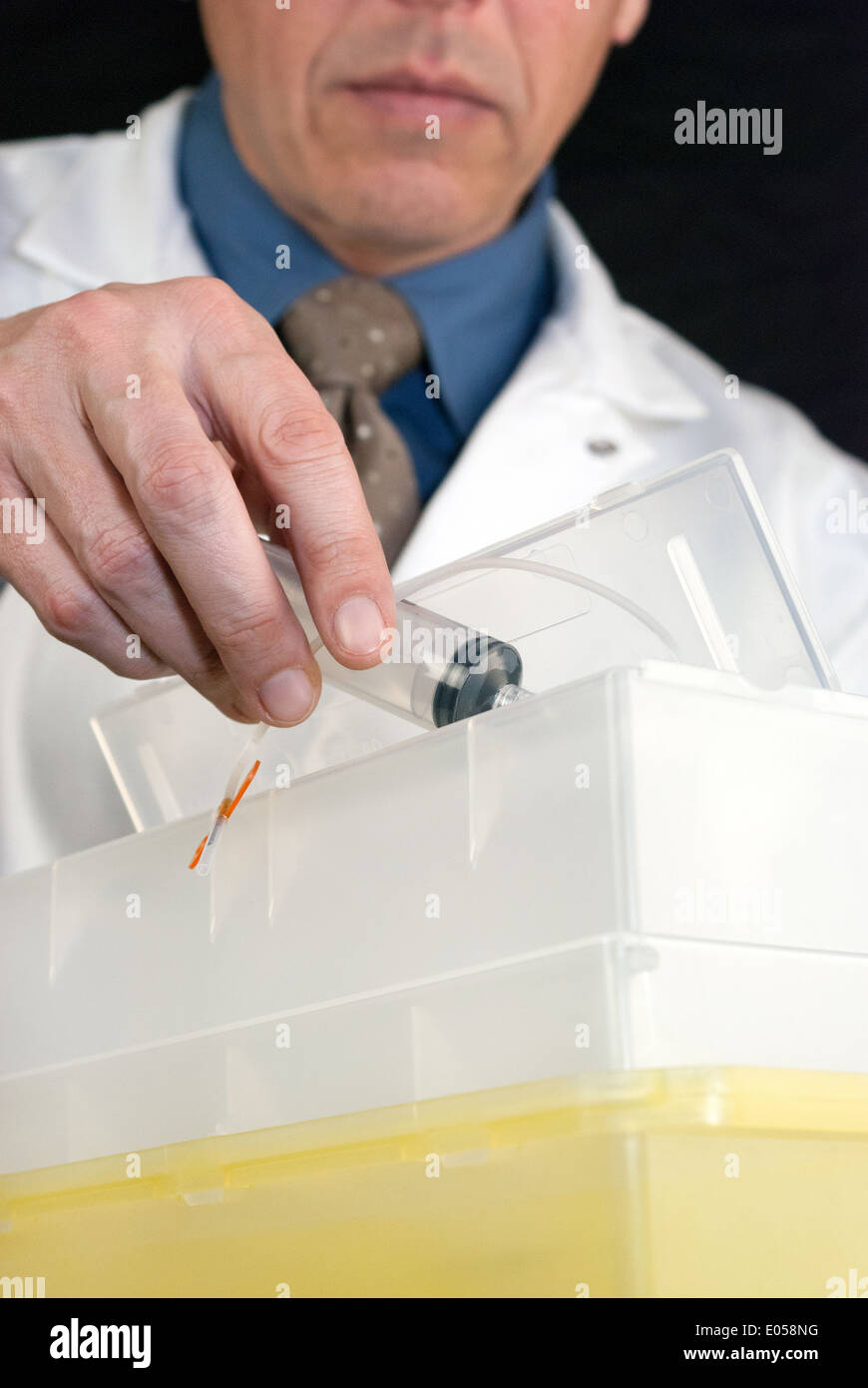 Close-up of a Doctor dropping a syringe with butterfly needle attached into sharps container. Stock Photo