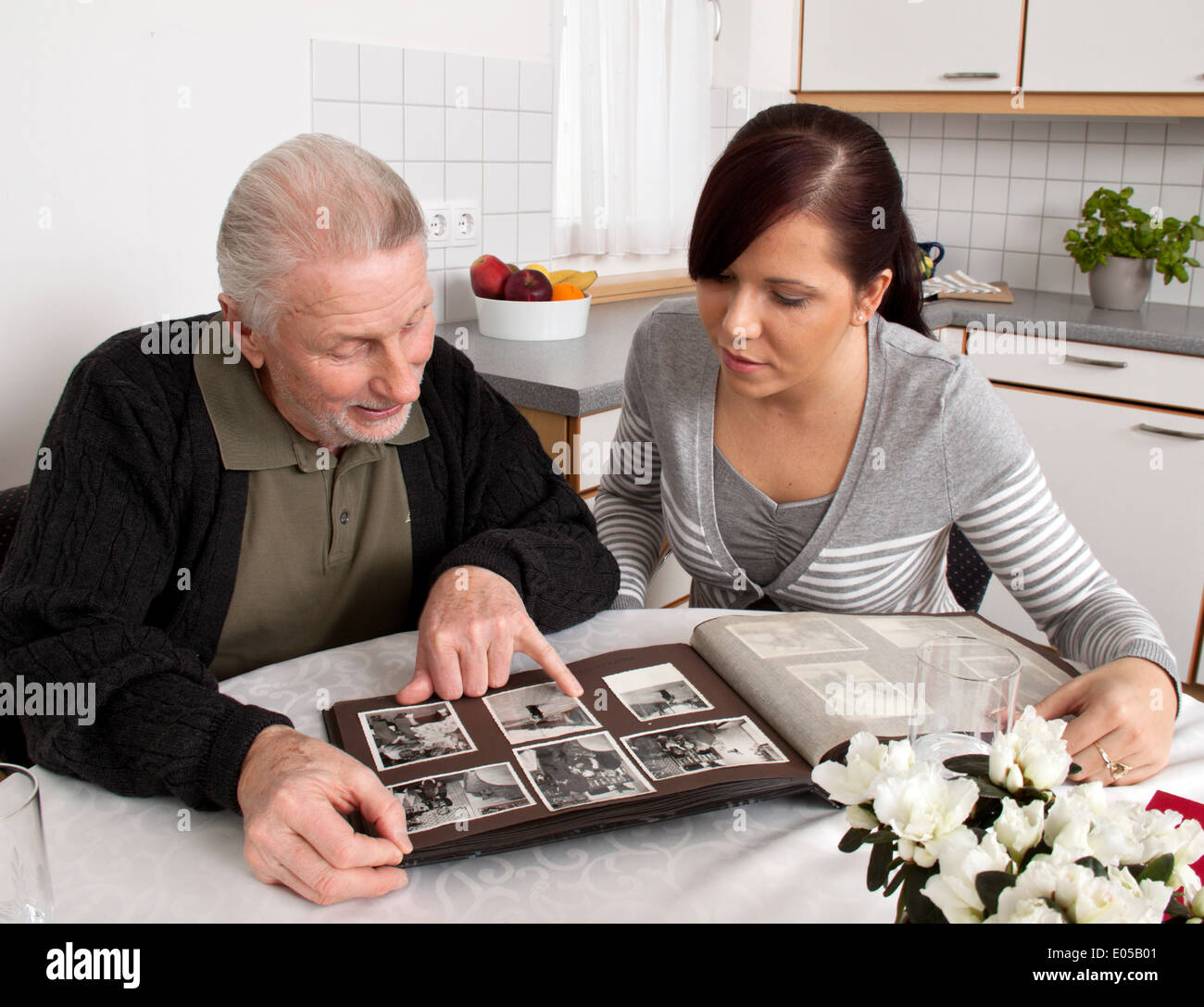 A young woman looks at a photo album with senior citizens, Eine junge Frau schaut mit Senioren ein Fotoalbum an Stock Photo