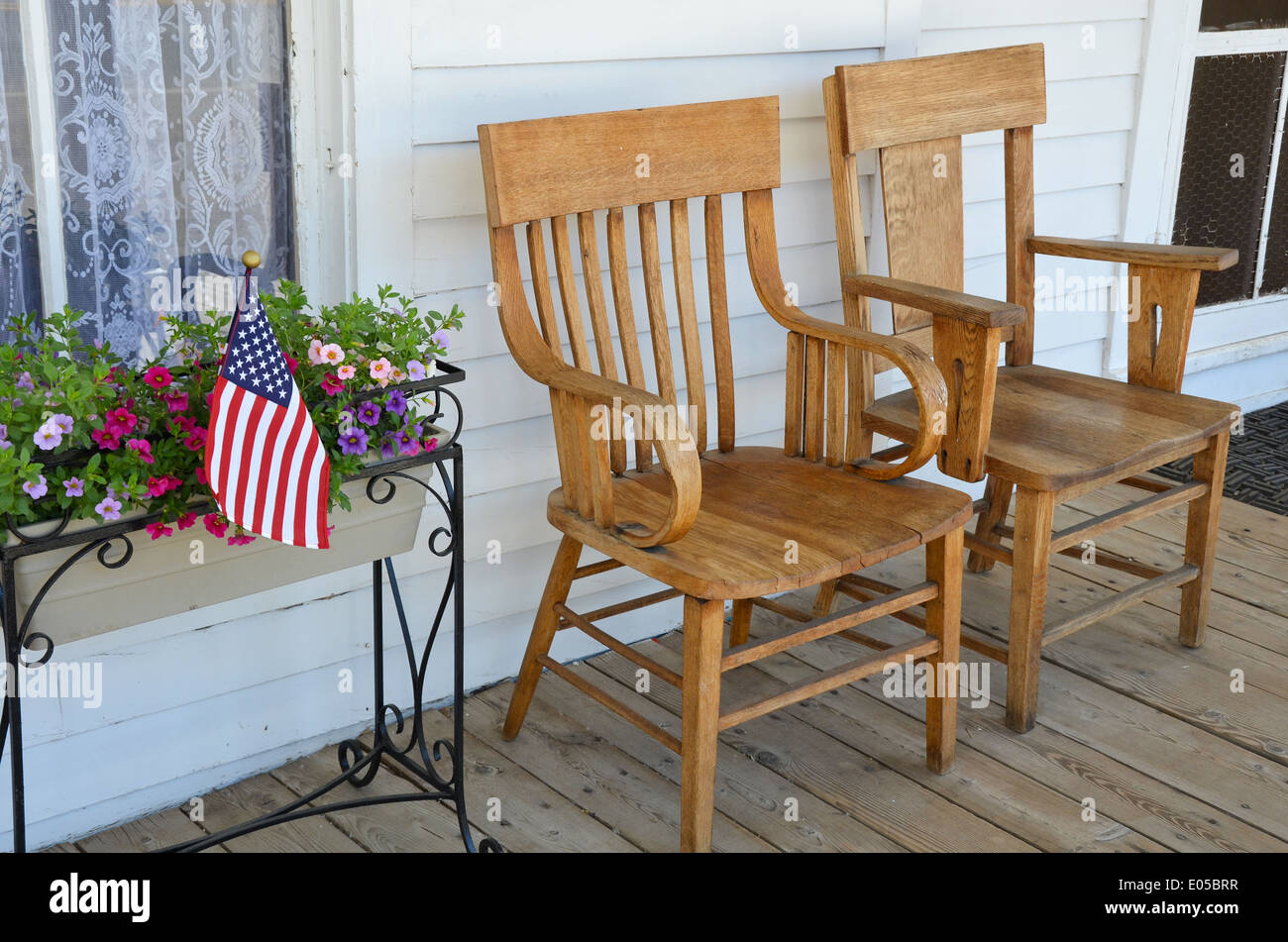 Two wooden chairs on old front porch with flowers and american flag ...