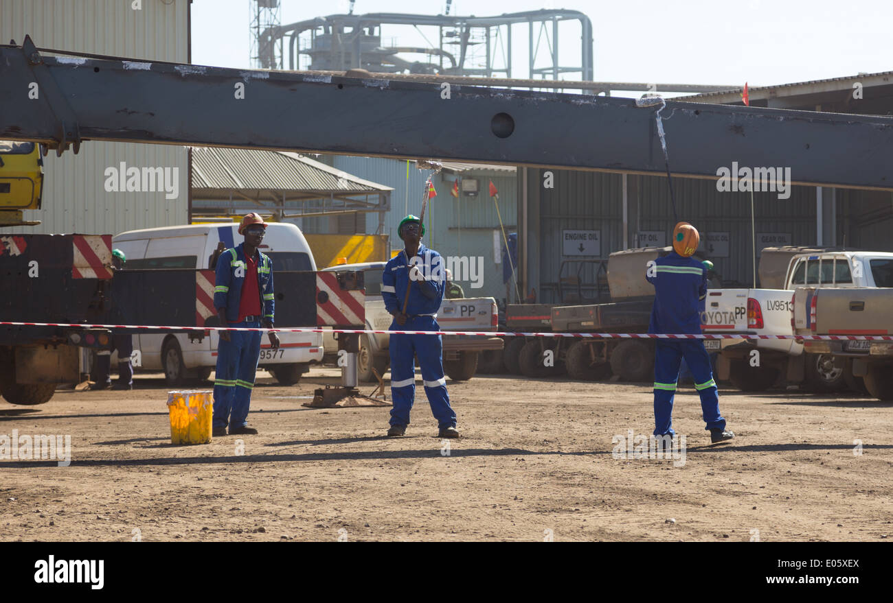 Three Zambian workers apply lubricant to a crane boom during routine