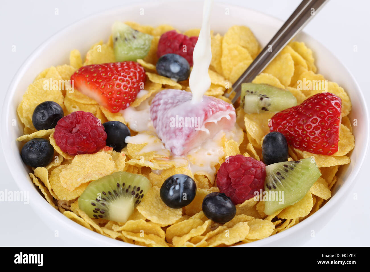 Milk pouring into fruit muesli with strawberries, raspberries, kiwi and blueberries Stock Photo