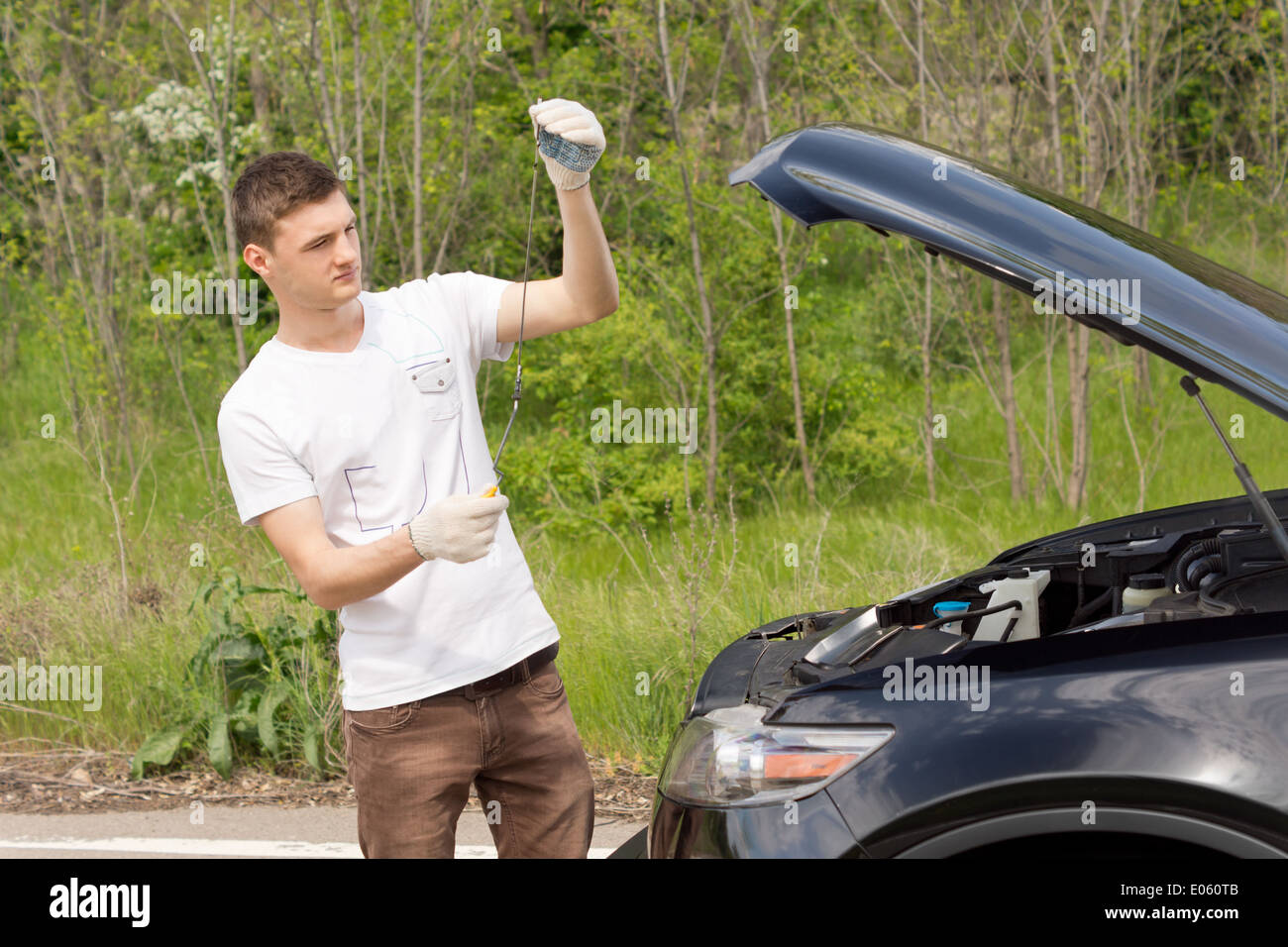 Mechanic checking the level of the oil on a car standing with the dipstick n his hand after the car broke down on a rural road Stock Photo